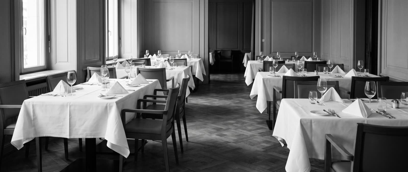 Salle de brasserie avant le service, nappes blanches et verres alignés.